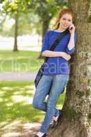 Redhead student leaning against a tree talking on the phone