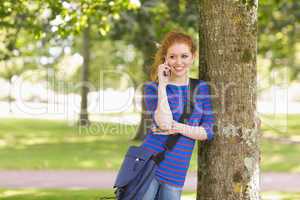 Happy student leaning against a tree talking on the phone