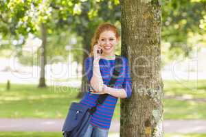 Cheerful student leaning against a tree talking on the phone