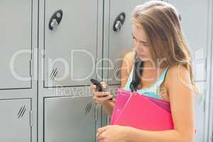 Smiling student sending a text beside lockers