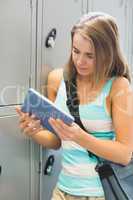 Happy student using her tablet beside lockers