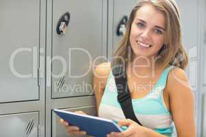 Cheerful student using her tablet beside lockers looking at came