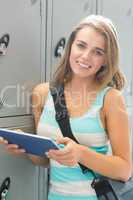 Happy student using her tablet beside lockers looking at camera