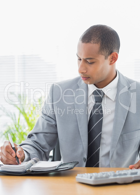 Businessman writing in diary at office desk