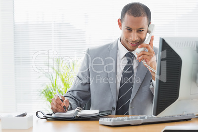 Smiling businessman using computer and phone at office