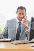 Smiling businessman using computer and phone at office