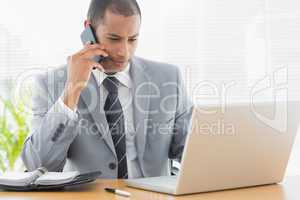 Businessman using laptop and cellphone at office