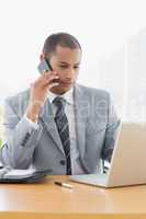 Businessman using laptop and cellphone at office