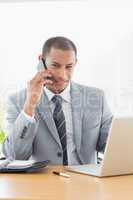 Smiling businessman using laptop and cellphone