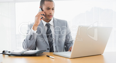 Concentrated businessman using laptop and cellphone