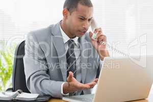 Concentrated businessman using laptop and phone