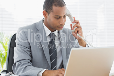 Concentrated businessman using laptop and phone