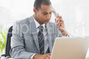 Concentrated businessman using laptop and phone