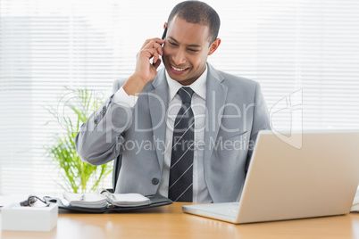 Smiling businessman with laptop using cellphone