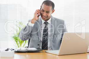 Smiling businessman with laptop using cellphone