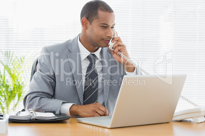 Businessman using laptop and phone at desk