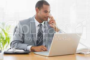 Businessman using laptop and phone at desk