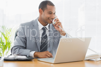 Businessman using laptop and phone at office desk