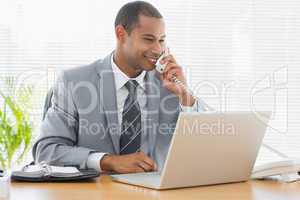 Businessman using laptop and phone at office desk