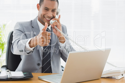 Businessman gesturing thumbs up while on call at desk