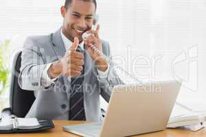 Businessman gesturing thumbs up while on call at desk