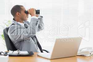 Businessman looking through binoculars at office desk
