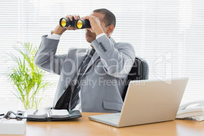 Businessman looking through binoculars at desk