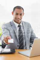 Well dressed man handing business card in front of laptop at off
