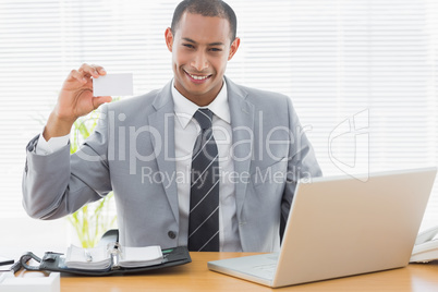 Confident well dressed man with business card at office desk