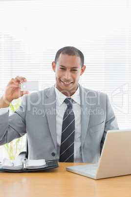 Confident well dressed man with business card at office desk