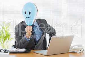 Businessman holding sad smiley faced balloon at office