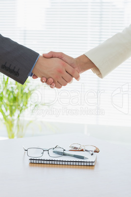 Close-up of shaking hands over eye glasses and diary