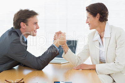 Smiling business couple arm wrestling at office desk