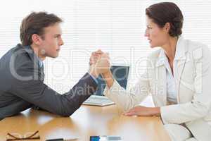 Serious business couple arm wrestling at office desk