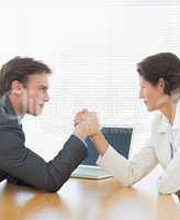 Business couple arm wrestling at office desk