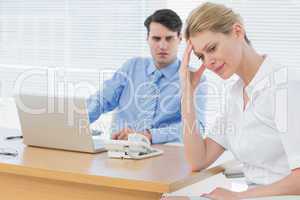 Upset businesswoman with man working on laptop