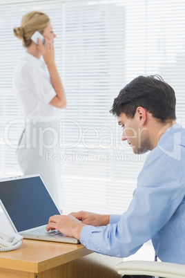 Businesswoman and man using cellphone and laptop at office