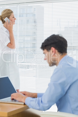 Businesswoman and man using cellphone and laptop at office