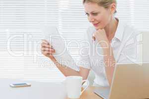 Businesswoman reading a document besides laptop at desk