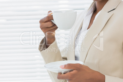 Mid section of elegant businesswoman with tea cup in office