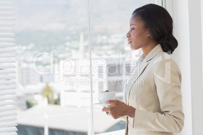 Elegant businesswoman with tea cup looking through office window