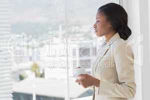 Elegant businesswoman with tea cup looking through office window