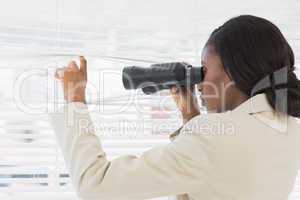 Businesswoman peeking with binoculars through blinds