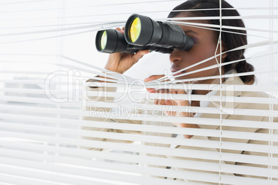 Businesswoman peeking with binoculars through blinds