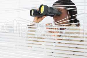 Businesswoman peeking with binoculars through blinds