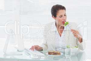 Businesswoman eating salad and using computer at desk