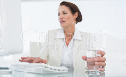 Businesswoman using computer while holding a glass of water