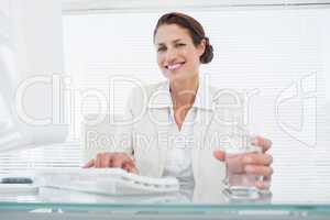 Businesswoman using computer while holding a glass of water