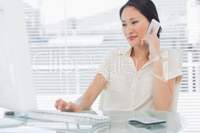 Businesswoman using cellphone and computer at desk