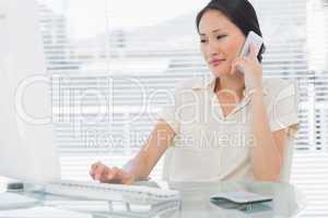 Businesswoman using cellphone and computer at desk